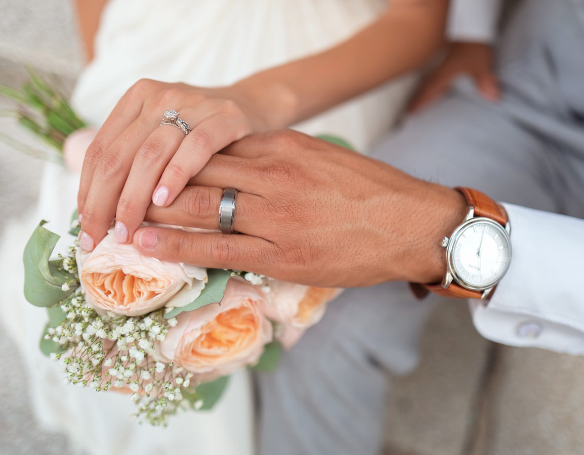 A close-up of a bride's hand over a groom's hand, resting on the bridal bouquet.