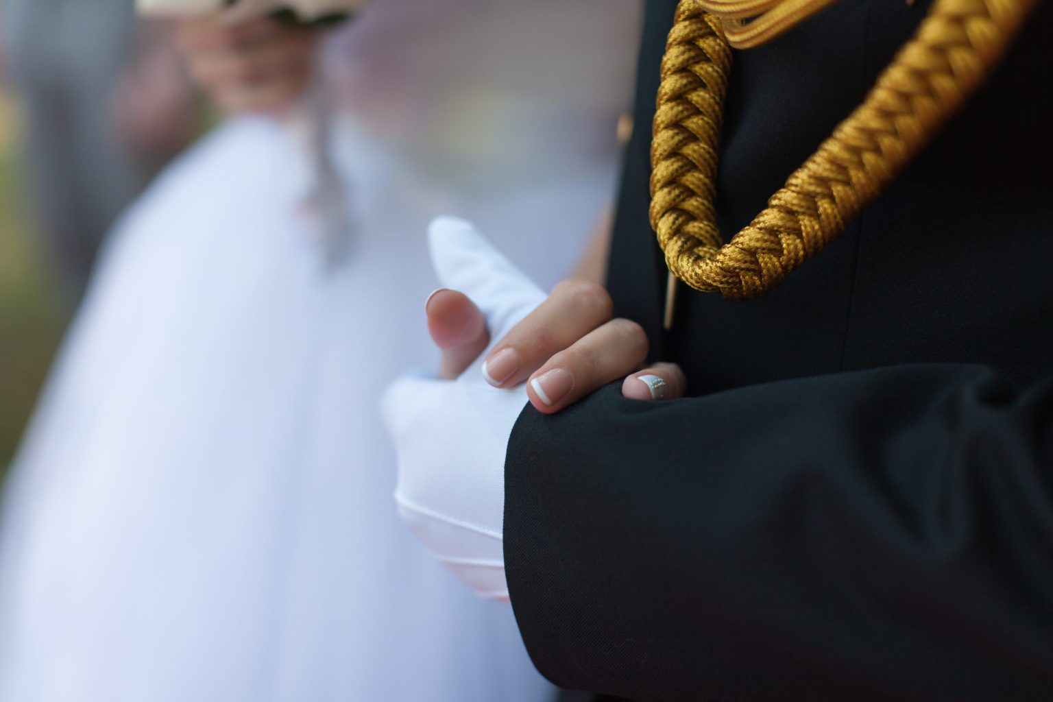 A groom in formal military attire holding hands with his bride.