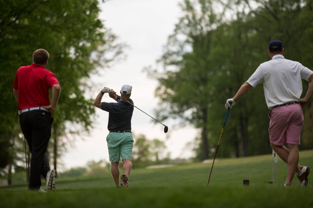 A golfer teeing off while two other golfers watch.