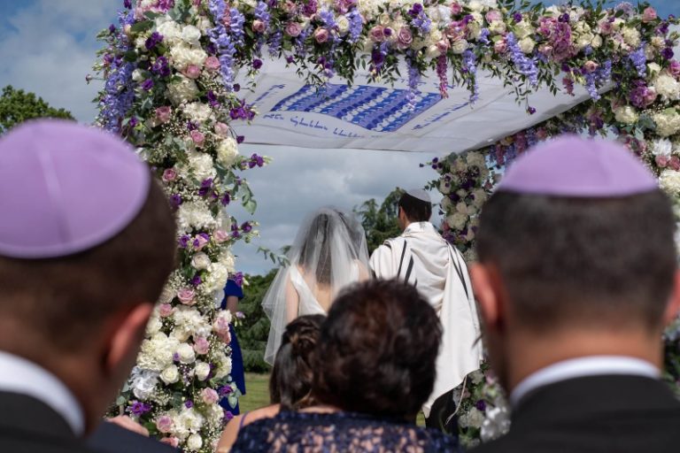Bride and groom under a Chuppah and an outdoor Jewish wedding.