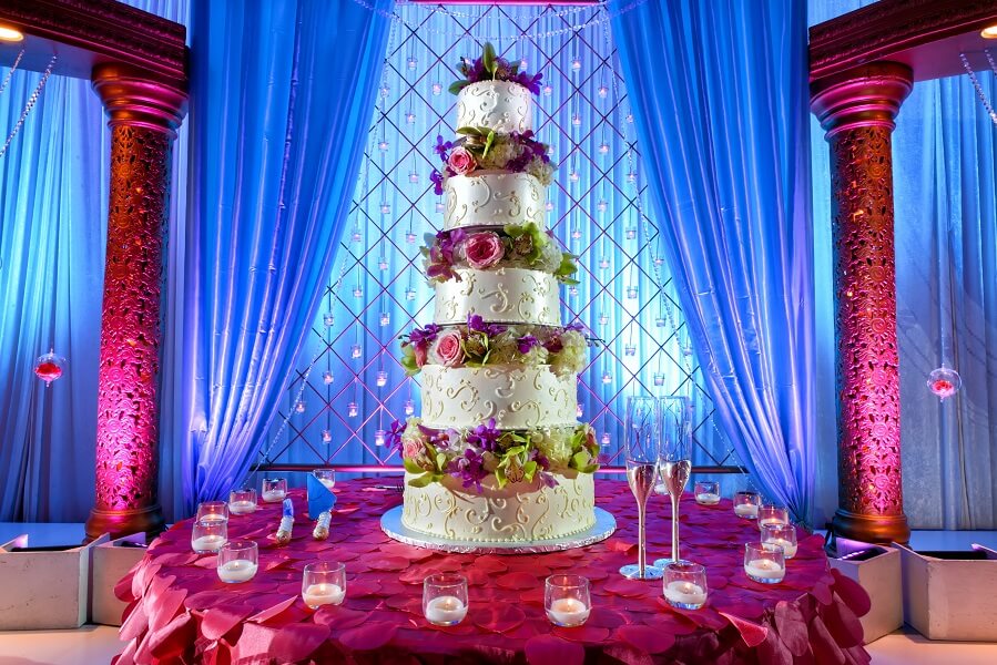 South Asian wedding cake on table with a magenta covering and surrounded by votive candles.