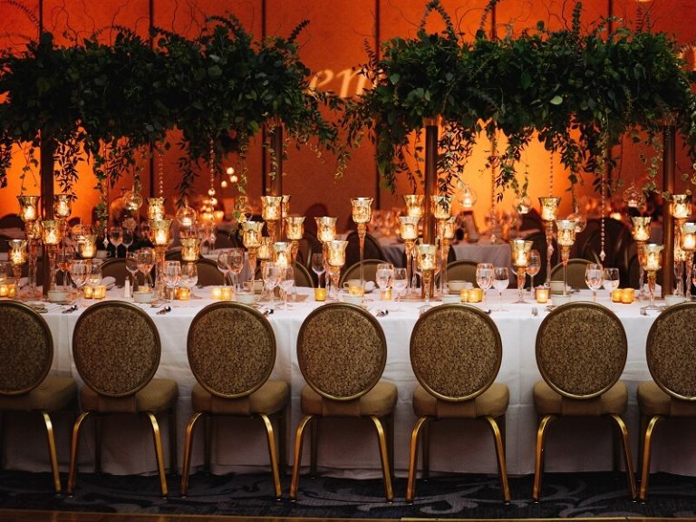 Long banquet table with candles and place settings at a South Asian wedding reception.